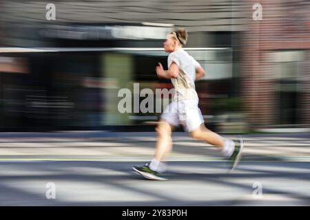 Junger Mann in heller Sportswear, der auf der Straße in der Stadt läuft, Bewegungsunschärfe, Schwenkfotografie Konzept für Sport als gesunde Freizeitaktivität, Co Stockfoto