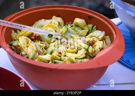 Tortellini-Salat in einer roten Plastikschale, hausgemacht für Picknick oder eine Party im Freien, ausgewählter Fokus, enge Tiefe des Feldes Stockfoto