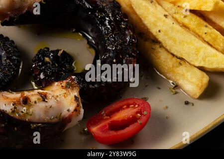 Gegrillte Kraken-Tentakel mit Kartoffeln und Kräutern auf einem Teller. Auf schwarzem Hintergrund. Stockfoto