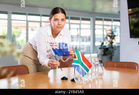 Vorbereitung der Geschäftspräsentation - Sekretärin platziert Flaggen von Australien und Südafrika auf den Verhandlungstisch Stockfoto