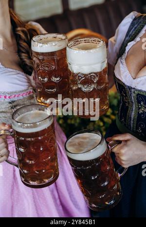 Frauen in traditionellen Dirndl-Kleidern, die auf dem Oktoberfest, dem deutschen Festival, mit Bierbecher toasten Stockfoto