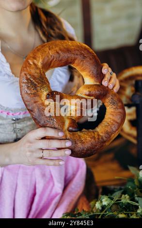 Traditionelle bayerische Brezel, gehalten von einer Frau in traditioneller Kleidung, perfekt für das Oktoberfest Stockfoto