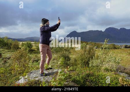 14. September 2024 Lofoten Islands, Norwegen weibliche Touristin macht ein iPhone (Smartphone) Foto auf der Autobahn E-10 in Grundstadveien, Nordland Stockfoto