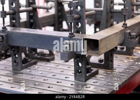 Klemmen fixieren die Werkstücke auf geschlitztem Schweißtisch. Selektiver Fokus. Stockfoto