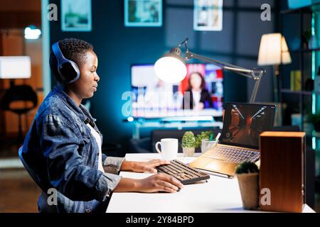 Junger afroamerikanischer Gamer nimmt an Online-Videospielturnieren Teil und genießt drahtloses Gaming auf einem Laptop. Konzentriert auf Bildschirm, Kopfhörer an, schwarze Frau zeigt ihre Fähigkeiten in der Wohnung. Stockfoto