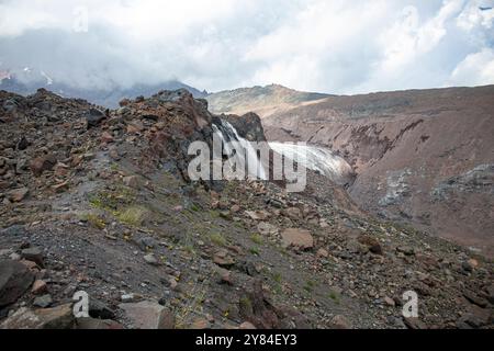Ein Wasserfall stürzt über eine felsige Klippe, umgeben von einer dramatischen Berglandschaft. Eine riesige und unberührte Wildnis mit hoch aufragenden Erbsen Stockfoto