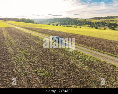 Black Car auf einer Landstraße zwischen Feldern in einer weiten ländlichen Landschaft, Car Sharing, VW ID5, Calw, Schwarzwald, Deutschland, Europa Stockfoto