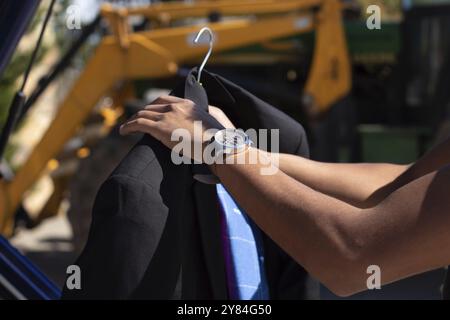 Nahaufnahme eines nicht erkennbaren latino-Mannes, der draußen eine amerikanische Jacke an einem Kleiderbügel platziert hat Stockfoto