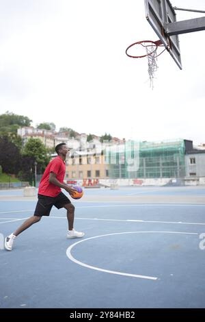 Vertikale volle Länge eines afroamerikanischen Basketballspielers, der auf einem Stadtplatz trainiert Stockfoto