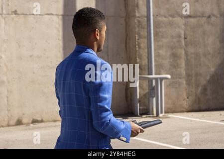 Rückansicht moderner lateinamerikanischer Geschäftsmann mit blauer Jacke und weißer Jeans mit Mappen unter freiem Himmel Stockfoto