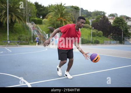 afrikanischer junger Mann in voller Länge, der auf dem Basketballfeld spielt und einen Ball dribbelt Stockfoto
