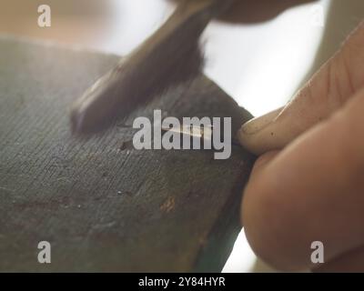 Nahaufnahme einer Person, die ein kleines Metallteil auf einer Werkbank putzt Stockfoto