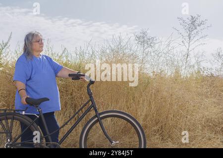 Übergewichtige Frau, im Profil gesehen, mit dem Fahrrad auf einem mit Vegetation bewachsenen Weg Stockfoto