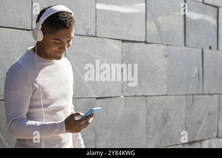 Mann genießt Musik über Kopfhörer mit seinem Telefon, horizontale Sicht mit Sonnenlicht Stockfoto