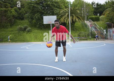 Porträt eines jungen Afro-Mannes, der einen Basketballball im Innenhof dribbelt Stockfoto