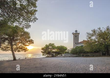 Wunderschöner Sonnenuntergang in einer Landschaft an einer felsigen Küste mit einem markanten Leuchtturm und Kiefernwald. Blick über die Küste zum Gebäude, auf den Mediterranea Stockfoto