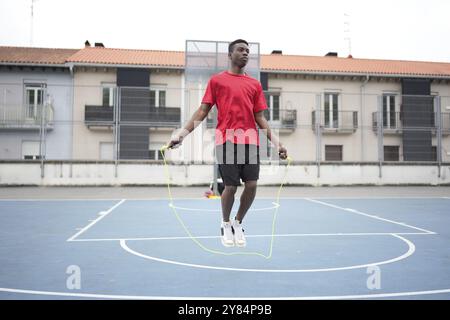 Ein junger afroamerikanischer Mann mit Sportkleidung springt auf einem städtischen Basketballfeld mit Seil Stockfoto