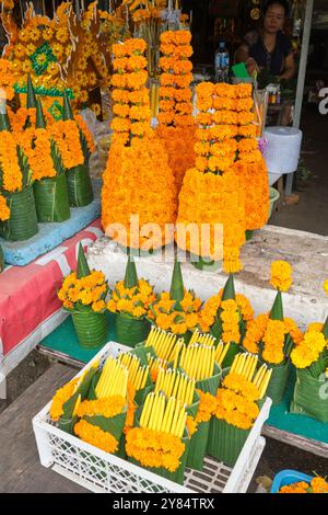 Orangefarbene Blumen und gelbe Kerzen, zum Verkauf in einem religiösen Geschäft, um sie als heilige Opfergaben in nahe gelegenen buddhistischen Tempeln zu verwenden. In Vientiane, Laos. Stockfoto