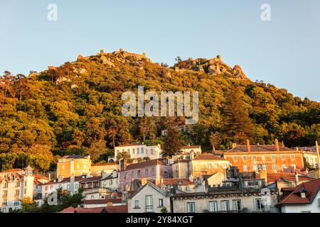 SINTRA, Portugal – die maurische Burg (Castelo dos Mouros) steht prominent auf einem Hügel über der Stadt Sintra mit dem goldenen Sonnenlicht am späten Nachmittag. Diese mittelalterliche Festung mit ihren Steinmauern, die sich entlang des Berges schlängeln, bietet eine dramatische Silhouette am Himmel und bietet einen beeindruckenden Blick auf die umliegende Landschaft. Stockfoto