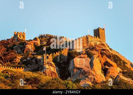 SINTRA, Portugal – die maurische Burg (Castelo dos Mouros) steht prominent auf einem Hügel über der Stadt Sintra mit dem goldenen Sonnenlicht am späten Nachmittag. Diese mittelalterliche Festung mit ihren Steinmauern, die sich entlang des Berges schlängeln, bietet eine dramatische Silhouette am Himmel und bietet einen beeindruckenden Blick auf die umliegende Landschaft. Stockfoto