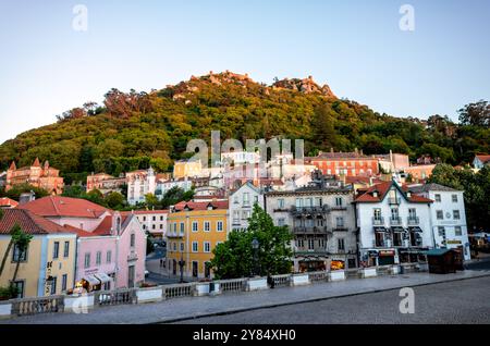 Maurisches Schloss Castelo dos Mouros Sintra Portugal // SINTRA, Portugal – das alte maurische Schloss (Castelo dos Mouros) steht auf einem Hügel mit Blick auf die historische Stadt Sintra. Die Festung wurde im 8. Und 9. Jahrhundert von den Mauren erbaut, die die iberische Halbinsel besetzten. Sie besteht aus Steinmauern, die sich entlang des bergigen Geländes schlängeln. Die zum UNESCO-Weltkulturerbe gehörende Stadt Sintra breitet sich im Vordergrund mit ihrer unverwechselbaren Architektur und den roten Ziegeldächern aus. Sintra liegt etwa 25 Kilometer westlich von Lissabon und ist bekannt für seine romantischen Paläste aus dem 19. Jahrhundert und Stockfoto