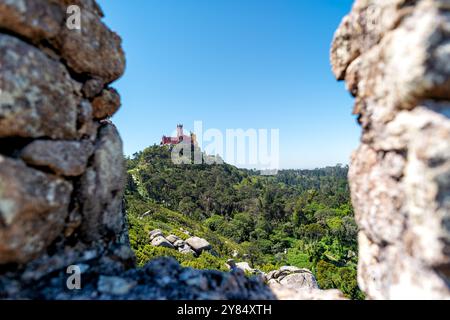 Pena-Palast Romantische Burgansicht vom maurischen Schloss Sintra-Berge Portugal | SINTRA, Portugal — Der Pena-Palast ist von den Mauern des Castelo dos Mouros (maurisches Schloss) aus sichtbar, seine eklektischen romantischen Türme erheben sich auf dem benachbarten Gipfel der Serra de Sintra. Der Palast wurde um 1840 von König Ferdinand II. geschaffen, der ein verfallenes Hieronymitenkloster in eine Fantasie umwandelte, die gotische, maurische, ägyptische und Renaissance-Elemente kombiniert — und es war derselbe König, der später die Mauern des maurischen Schlosses als malerische Ruine in seine komponierte romantische Landschaft einband. Das Caste Stockfoto