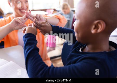 In der Schule spielte eine Lehrerin und ein afroamerikanischer Junge Gebärdensprache, lächelte und hatte Spaß Stockfoto