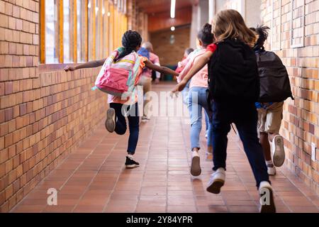 Sie laufen im Schulflur, eine Gruppe von verschiedenen Kindern mit Rucksäcken auf dem Weg zum Unterricht Stockfoto