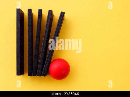Rote Kugel, die mehrere Holzfiguren in einer Reihe schiebt Stockfoto