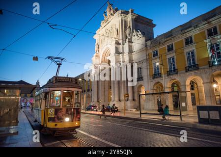 Arco da Rua Augusta Tram Lissabon Portugal // LISSABON, Portugal — Eine Straßenbahn fährt in der Abenddämmerung vor dem Arco da Rua Augusta auf der Praca do Comércio. Der Prac do Comércio ist ein historischer Platz im Stadtteil Pombaline in Lissabon, direkt am Fluss Tejo. Der Triumphbogen wurde errichtet, um an den Wiederaufbau der Stadt nach dem verheerenden Erdbeben von 1755 zu erinnern, das einen Großteil von Lissabon zerstörte. Die skulpturale Gruppe, die den Bogen krönt, repräsentiert Glory Belohnung Tapferkeit und Genie. Der Platz ist einer der wichtigsten öffentlichen Bereiche von Lissabon und ein großer Platz Stockfoto
