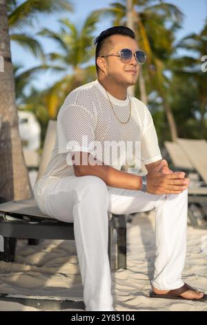 Jugendmode eines Mannes in einem Resort mit wunderschönem Strand, natürliche Landschaft an einem Sommertag, trägt Sonnenbrille, T-Shirt, Personenporträt, Model Stockfoto