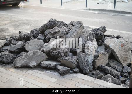 Über die städtische Straße verstreut gibt es Haufen von gebrochenem Asphalt, was auf laufende Bauarbeiten hinweist Stockfoto