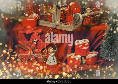 Traditionelle Weihnachtsdekorationen auf rotem Hintergrund. Keramikfiguren, Geschenkboxen mit Hirsch, ein künstlicher Weihnachtsbaum für Weihnachtsgeschenke. Stockfoto