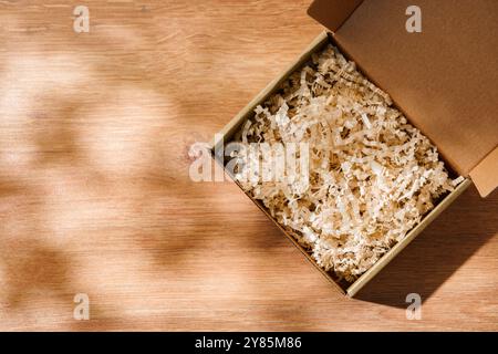 Öffnen Sie den Karton mit geschredderter Papierfüllung auf einem Holztisch Stockfoto