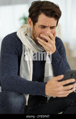 Ein Mann, der durch die Nachricht auf seinem Smartphone zu Tränen gebracht wurde Stockfoto