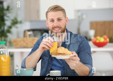 Mann am Frühstückstisch, der ein Croissant anbietet Stockfoto