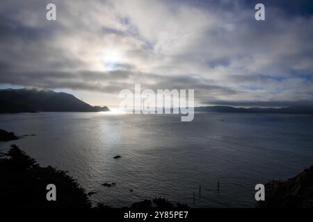 Helle Sonne und dunkle Wolken über der Küste mit Brücke und Stadt in der Ferne Stockfoto