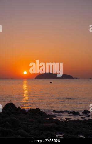 Ein ruhiger Sonnenaufgang über Jamjindo Island, Incheon. Die Sonne reflektiert vom ruhigen Meer und wirft einen goldenen Pfad mit Felsen im Vordergrund. Stockfoto