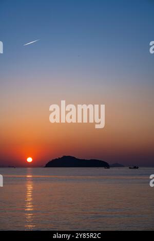 Ein friedlicher Sonnenaufgang auf Jamjindo Island, Incheon. Die goldene Sonne spiegelt sich auf dem ruhigen Meer, mit Fischerbooten, die die ruhige Aussicht verbessern. Stockfoto