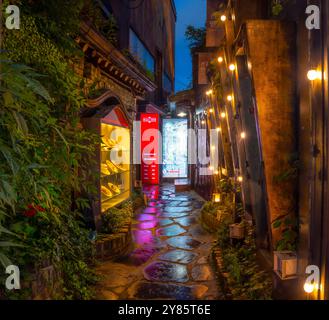 Malerische Gasse in Insadong, Seoul, beleuchtet von warmen Abendlichtern. Der nasse Steinweg reflektiert das sanfte Leuchten und schafft eine gemütliche Atmosphäre. Stockfoto