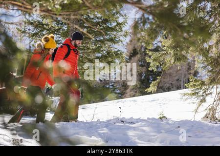 Bergsteigerpaar wandern durch einen verschneiten Wald mit Bergen im Hintergrund, Wintersaison Stockfoto