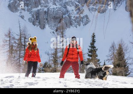 Ein Paar wirft Schneebälle auf ihren Hund, während sie gemeinsam einen Tag in den Bergen verbringen Stockfoto