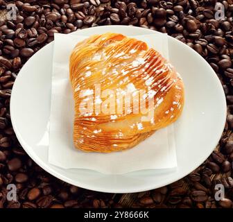 Köstliches, traditionelles Sfogliatella-Gebäck, mit Puderzucker bestäubt, serviert auf weißem Teller über Kaffeebohnen Hintergrund Stockfoto