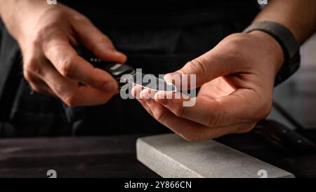 Männerhände mit Klappmesser und Schleifsteinwerkzeug. Meisterspitzmesser auf einem Schleifstein Stockfoto