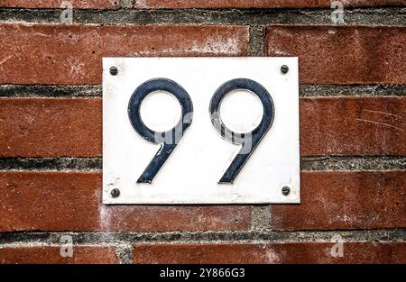 Adressschild an der Ziegelmauer des Wohngebäudes mit der Nummer neunundneunzig. Hausausweisschild Stockfoto