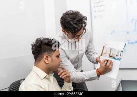 Ein Immobilienmakler erklärt einem potenziellen Kunden in der Buchungsstelle die Details eines neuen Wohnprojekts. Das Bild erfasst den Moment o Stockfoto