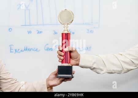 Nahaufnahme von Händen mit Trophäe, die Leistung und Exzellenz bei der Erbringung von Dienstleistungen symbolisieren. Die Trophäe stellt die Anerkennung für „Outstand“ dar Stockfoto