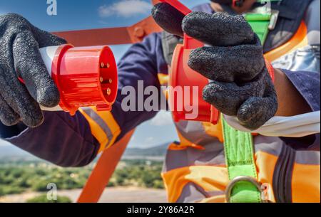 Elektriker aus der Vogelperspektive hoch oben auf dem Turm, Hochspannungsstecker in der Hand. Anschluss eines 380-Volt-Hochspannungs-, Dreiphasen-Steckers, Stromkosten, elektr Stockfoto