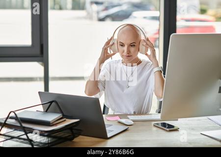 Eine junge kahlköpfige Frau ist in ihre Arbeit an einem modernen Schreibtisch vertieft und trägt elegante Kleidung und Kopfhörer. Stockfoto