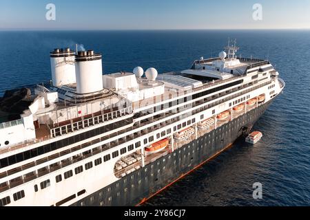 Großes Kreuzfahrtschiff, das an einem sonnigen Tag auf dem Meer segelt, mit einem Rettungsboot auf dem Wasser Stockfoto